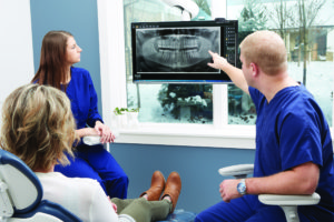 An Endodontics dentist reviewing a 3D imaging scan with a patient and hygienist.